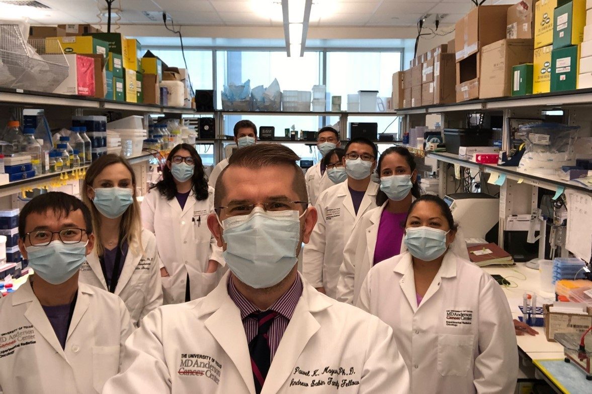 Mazur group in medical masks and white lab coats, standing between two benches in a wet lab