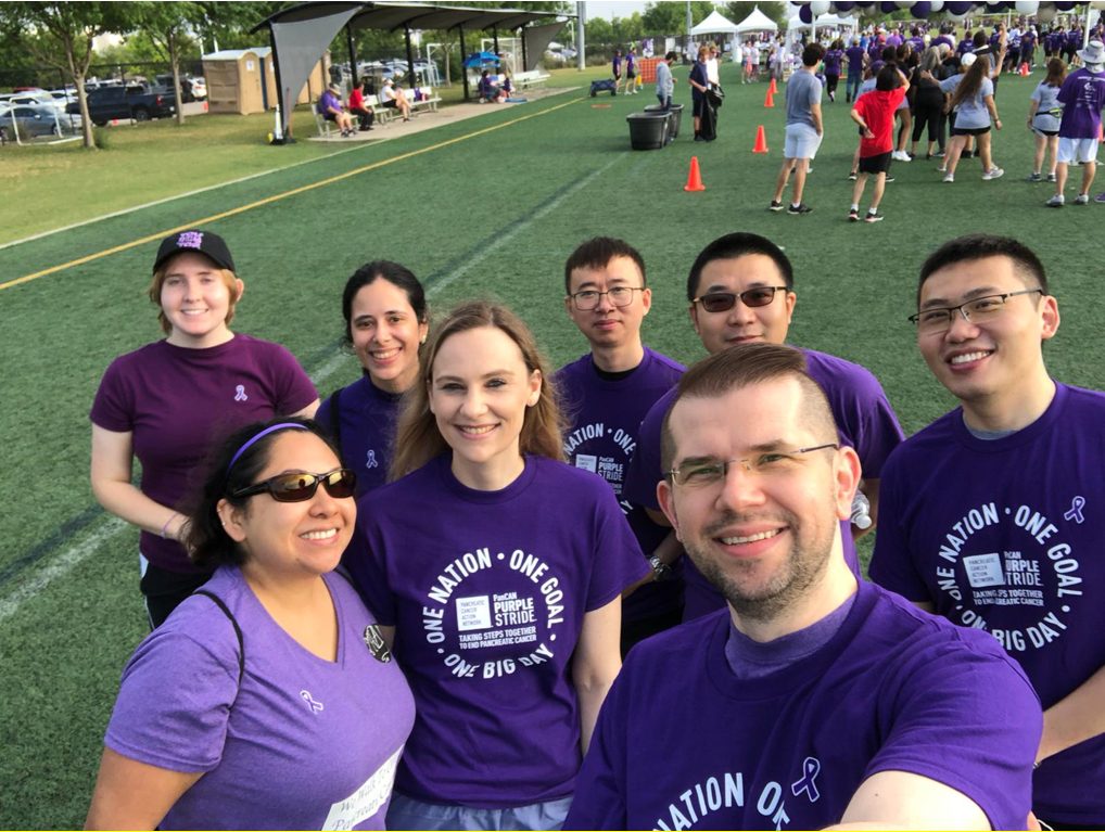 Selfie of eight Mazur group members in purple shirts, standing on a soccer field