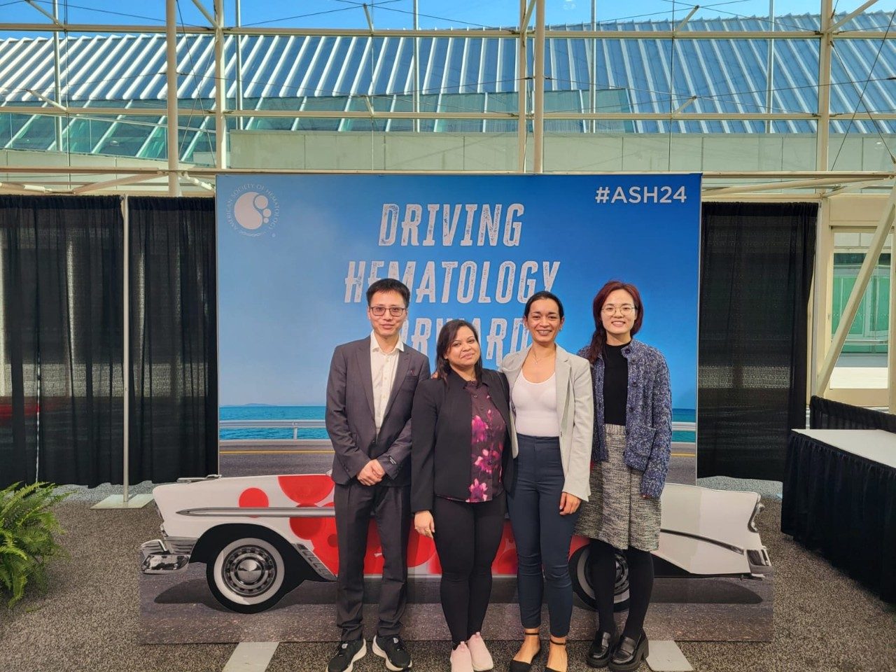 Four people posed in front of a fake car