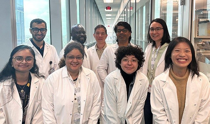 9 people wearing white coats stand in a hallway