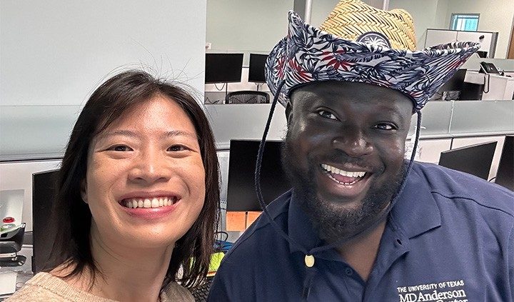 Two people pose in front of monitors, one wearing a cowboy hat
