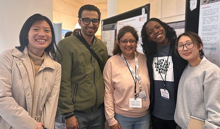 Photo of five Pan Lab members posing in front of scientific posters.