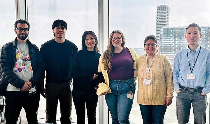 Six people stand in front of a window
