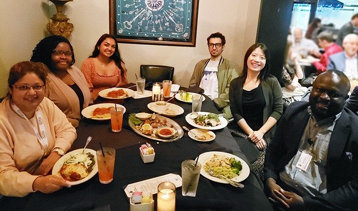 Six people sit around a table of food indoors