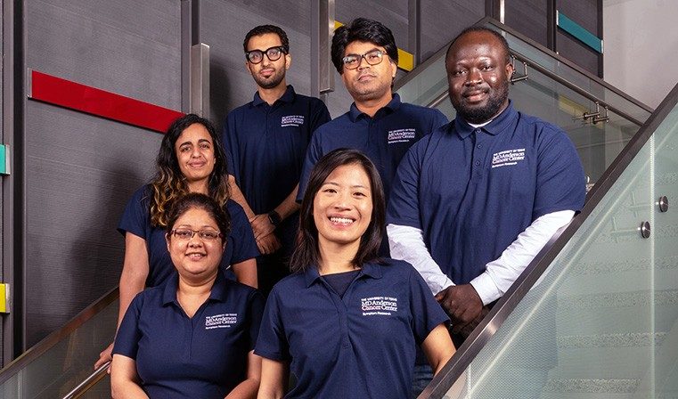 Six people wearing MD Anderson polo shirts pose on a flight of stairs