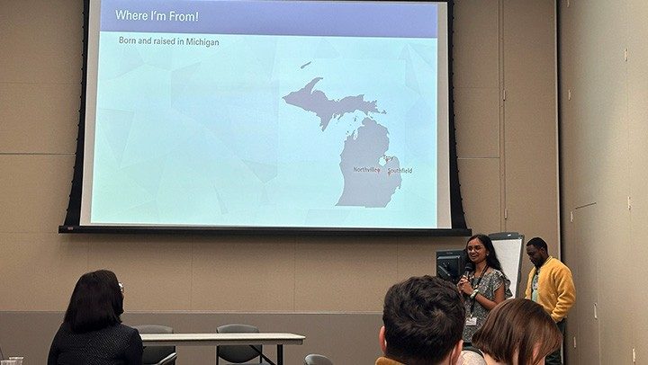 Person standing at podium with a slide projected on the wall behind her