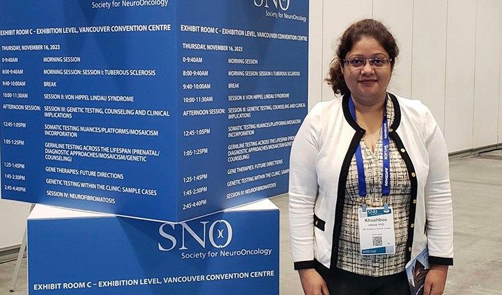 Photo of Pan Lab member Khushboo Irshad standing next to a sign