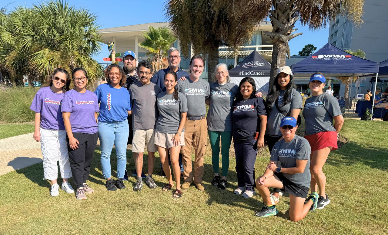13 people pose outside in front of palm trees and an MD Anderson branded tent