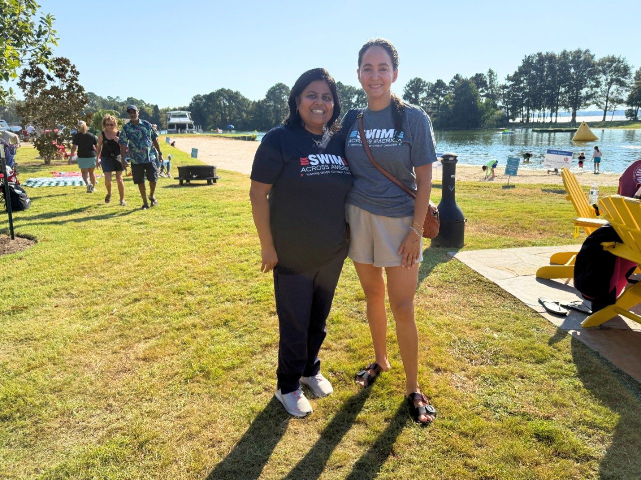 Two people pose on grass outside near water