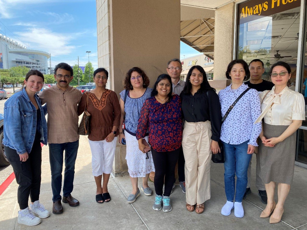 Ten people in a row, posing for a photo outside in a strip mall
