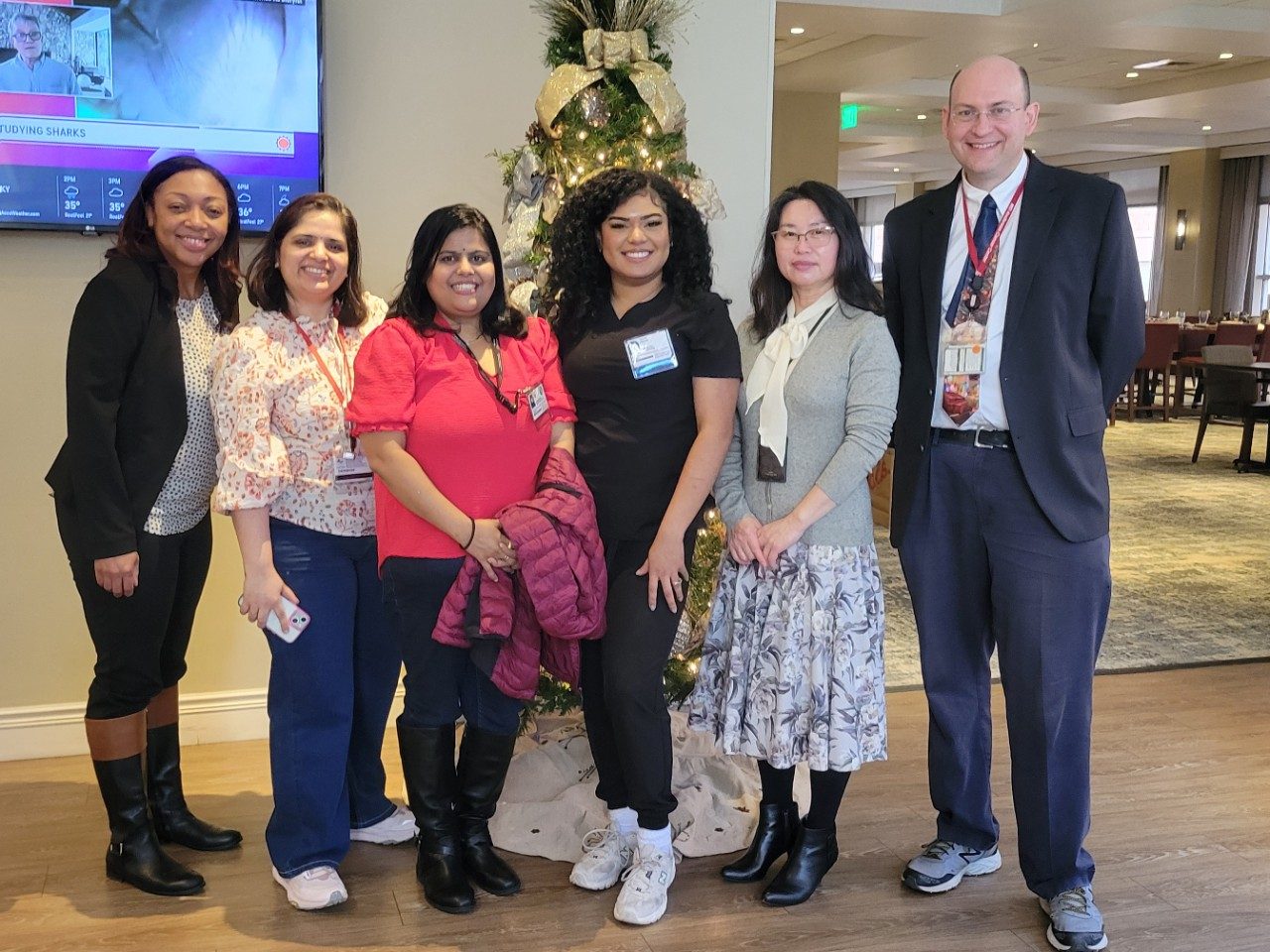Six people lined up in a row in a lobby, posing for a photo