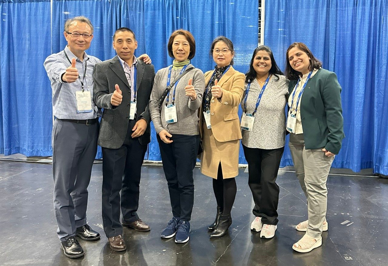 Six lab members pose in a line in front of a blue curtain backdrop