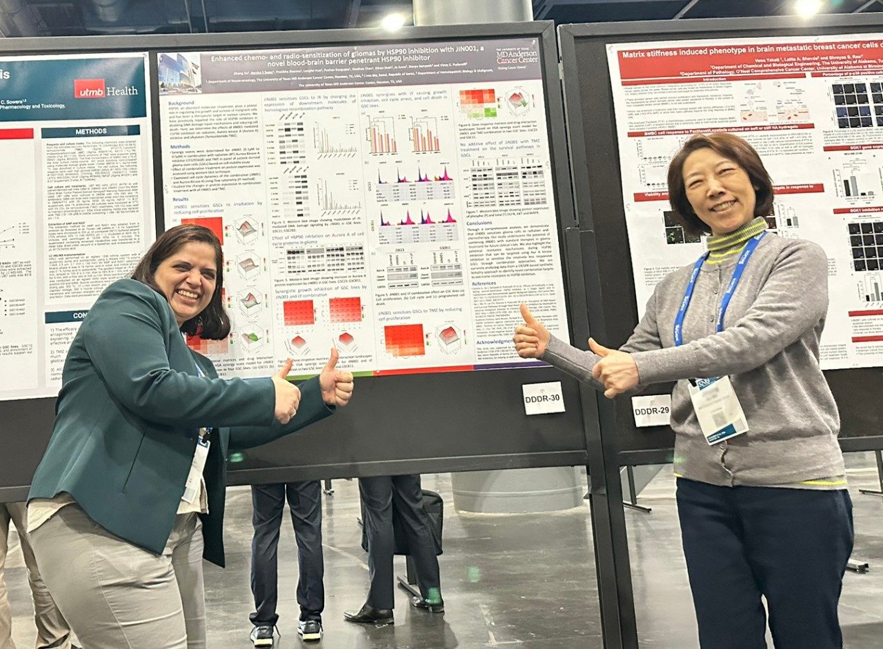 Two women posed on either side of a poster giving thumbs up