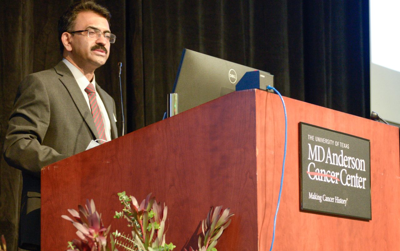 Dr. Puduvalli behind a podium with an MD Anderson logo on it and flowers in the foreground