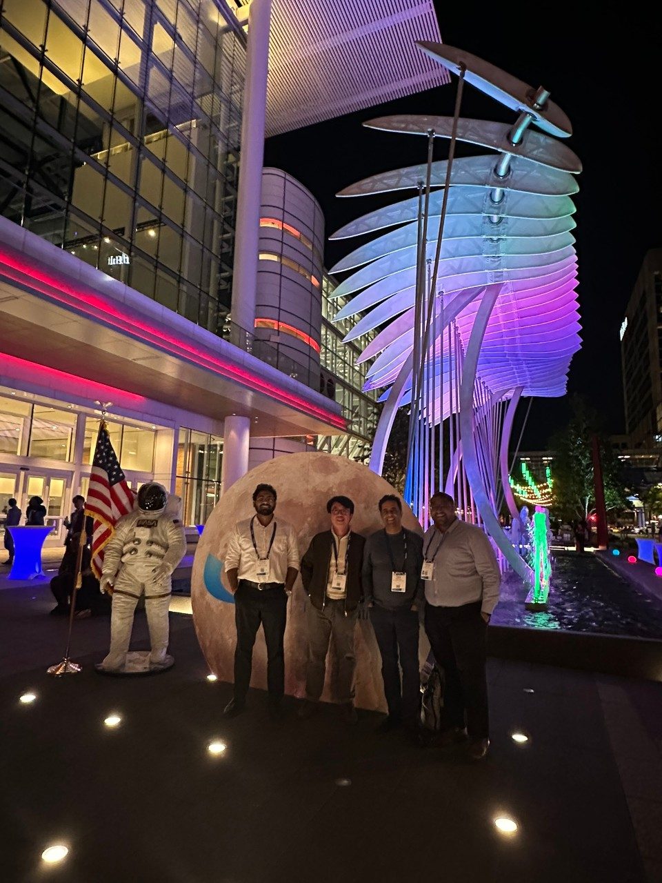 Four lab members pose in front of a moon and astronaut photo op