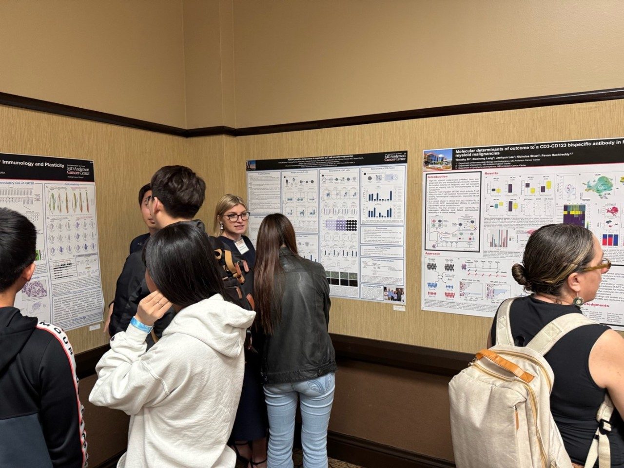 Woman presenting poster to attendees, who are listening and looking at the poster