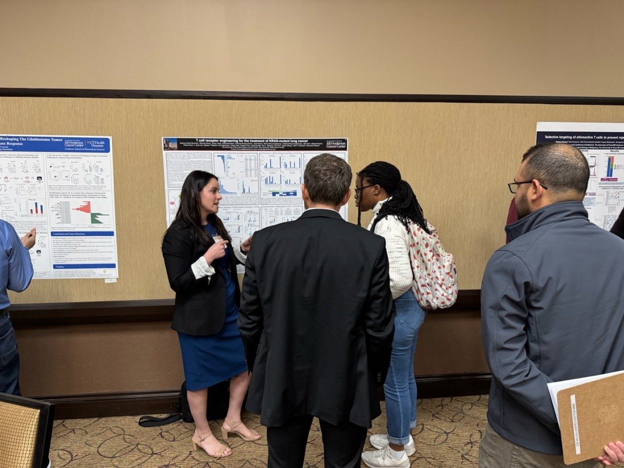 Woman presenting poster to attendees, who are listening and looking at the poster