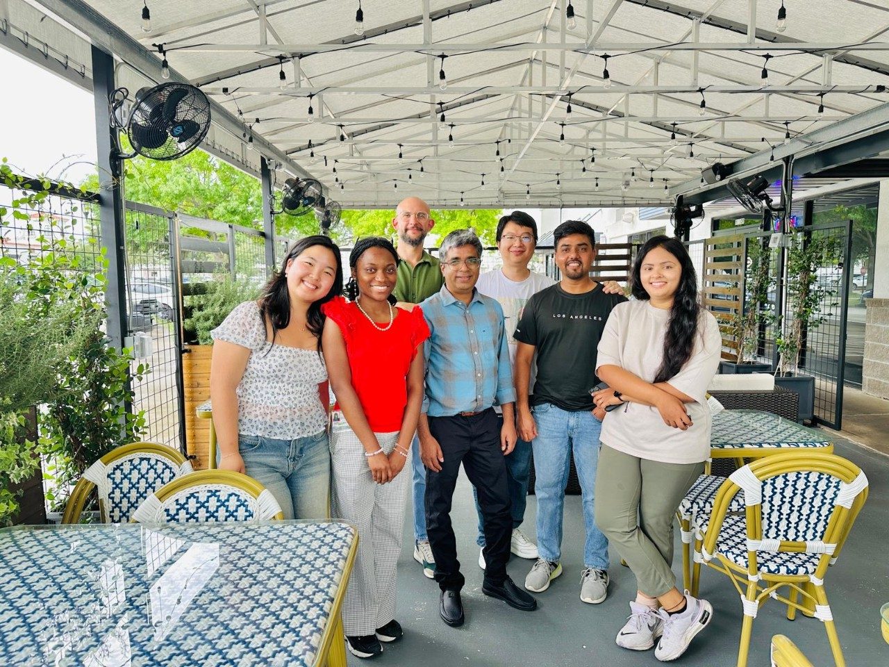 Seven people posing in the outdoor section of a restaurant