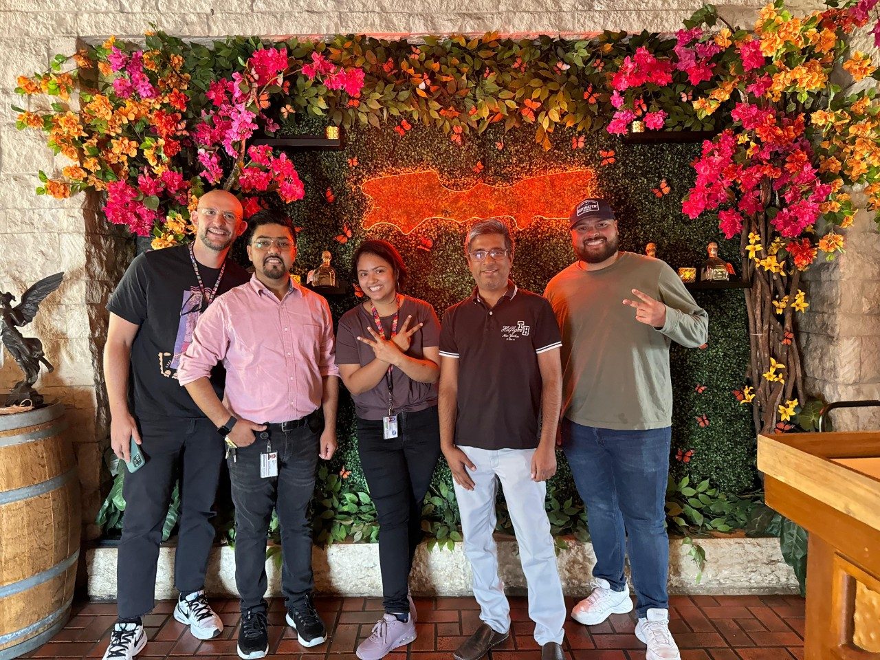 Five people standing in front of a flower and greenery photo backdrop wall