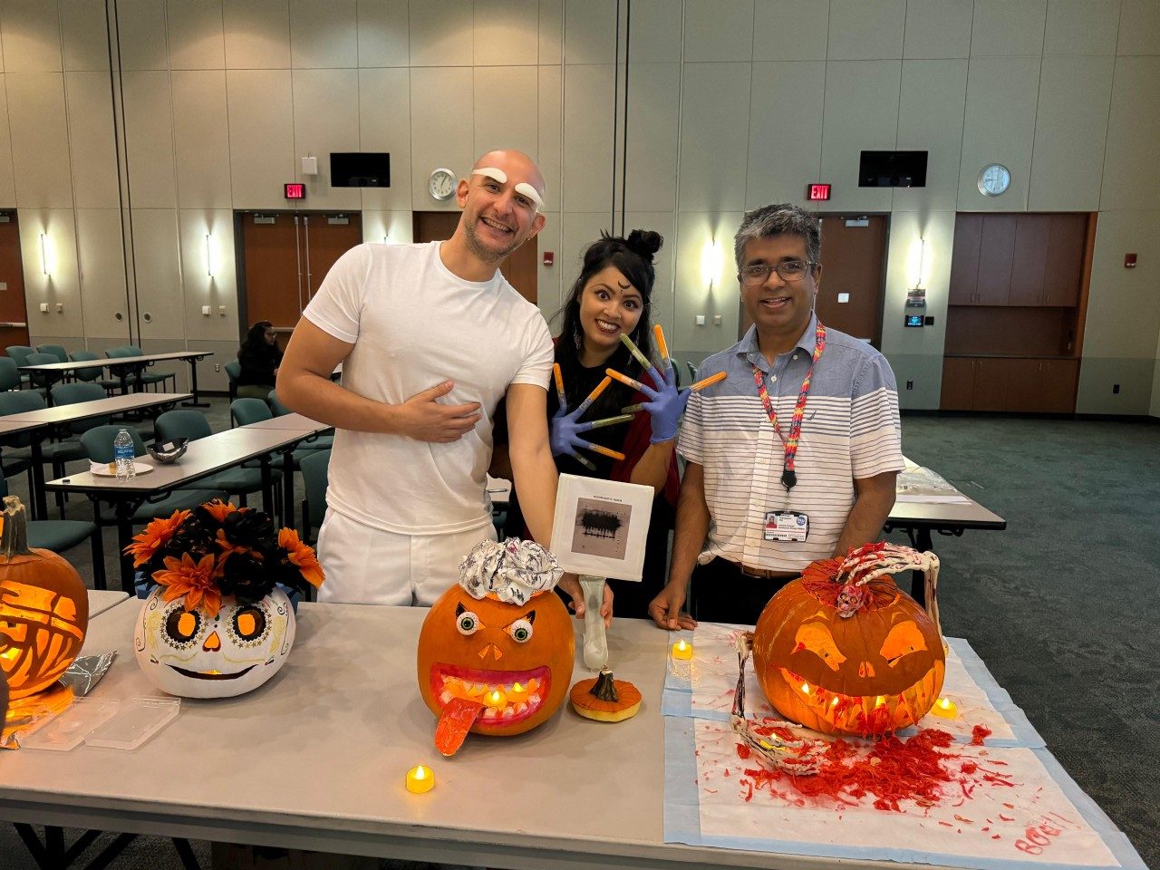 Three lab members posed with painted or carved pumpkins