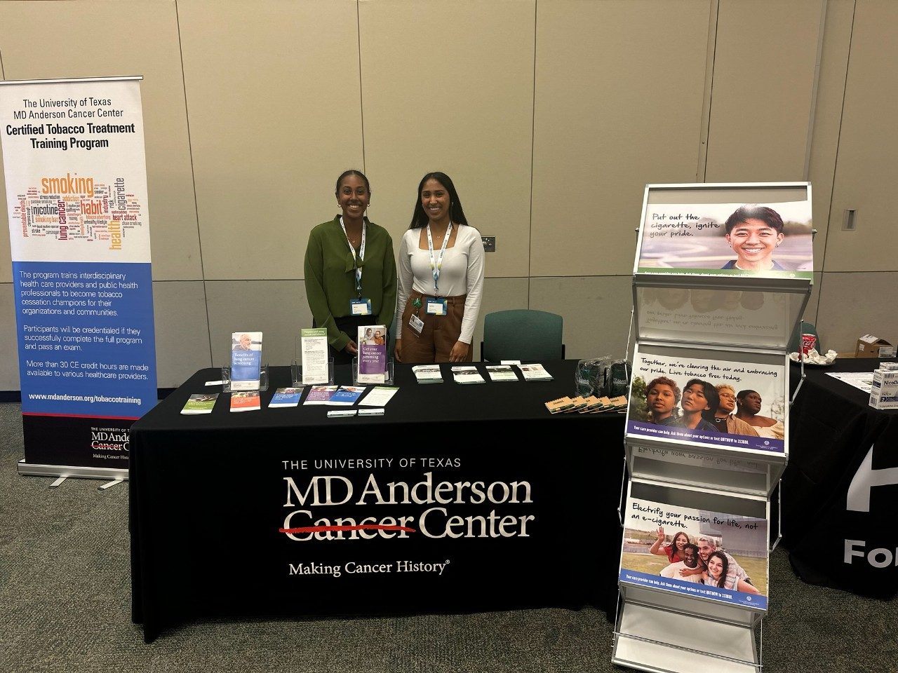 Two young women behind an MD Anderson table next to a sign for the Certified Tobacco Treatment Training Program