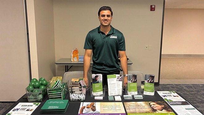 One person stands behind a table with brochures and other materials