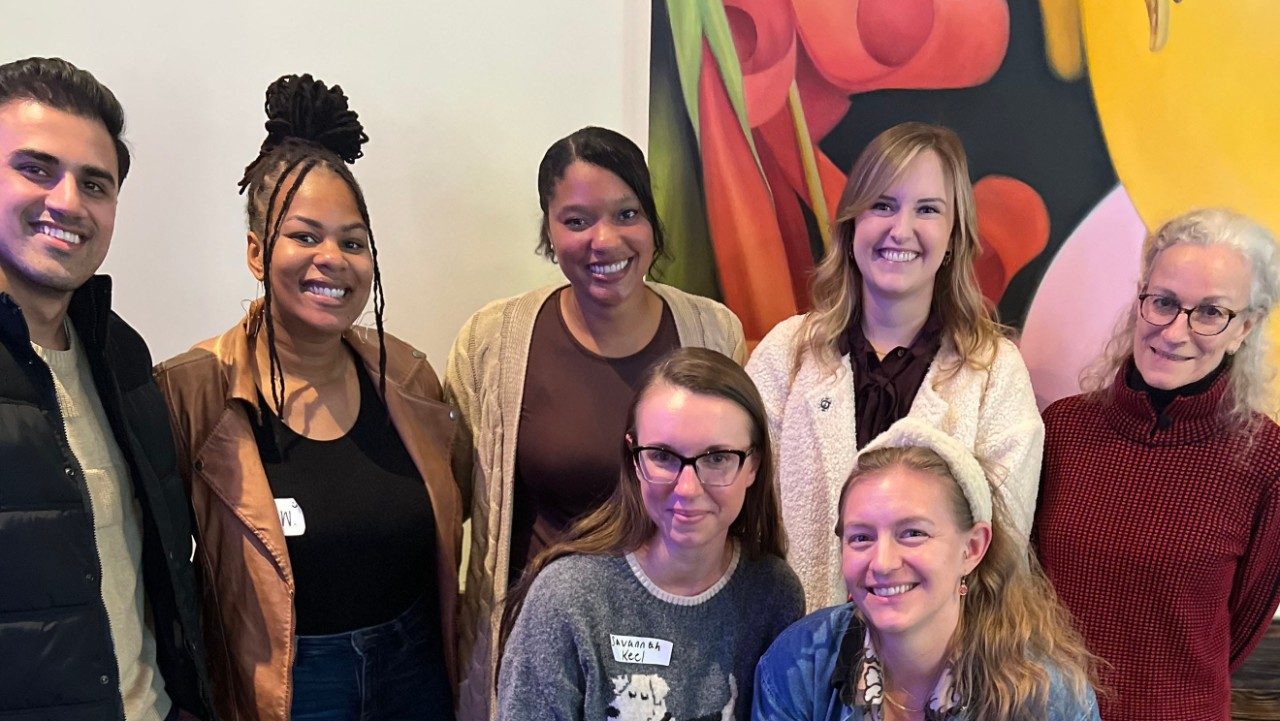 Group photo of 7 people in front of a piece of artwork