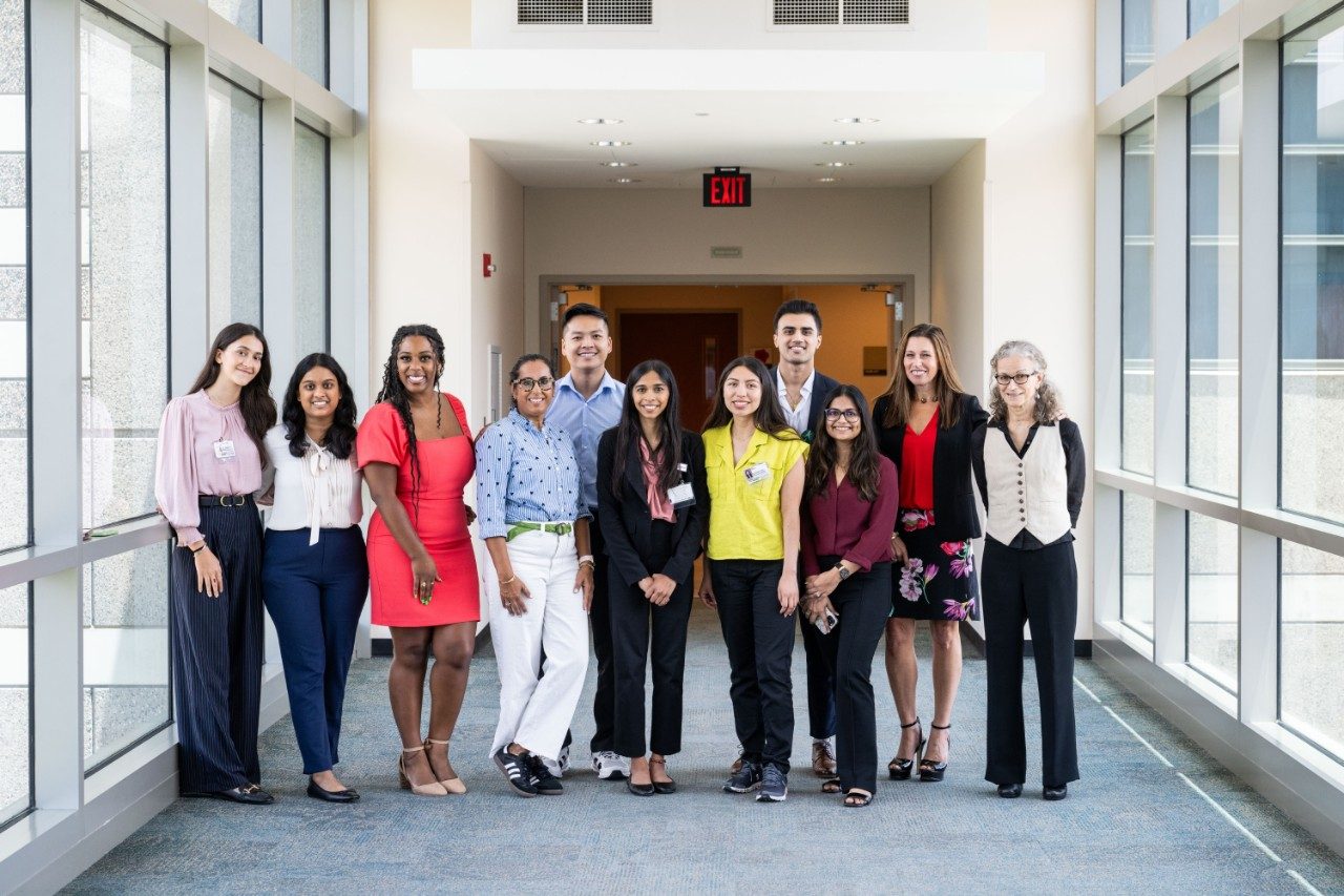 Row of people posing in a hallway at MD Anderson lined with windows