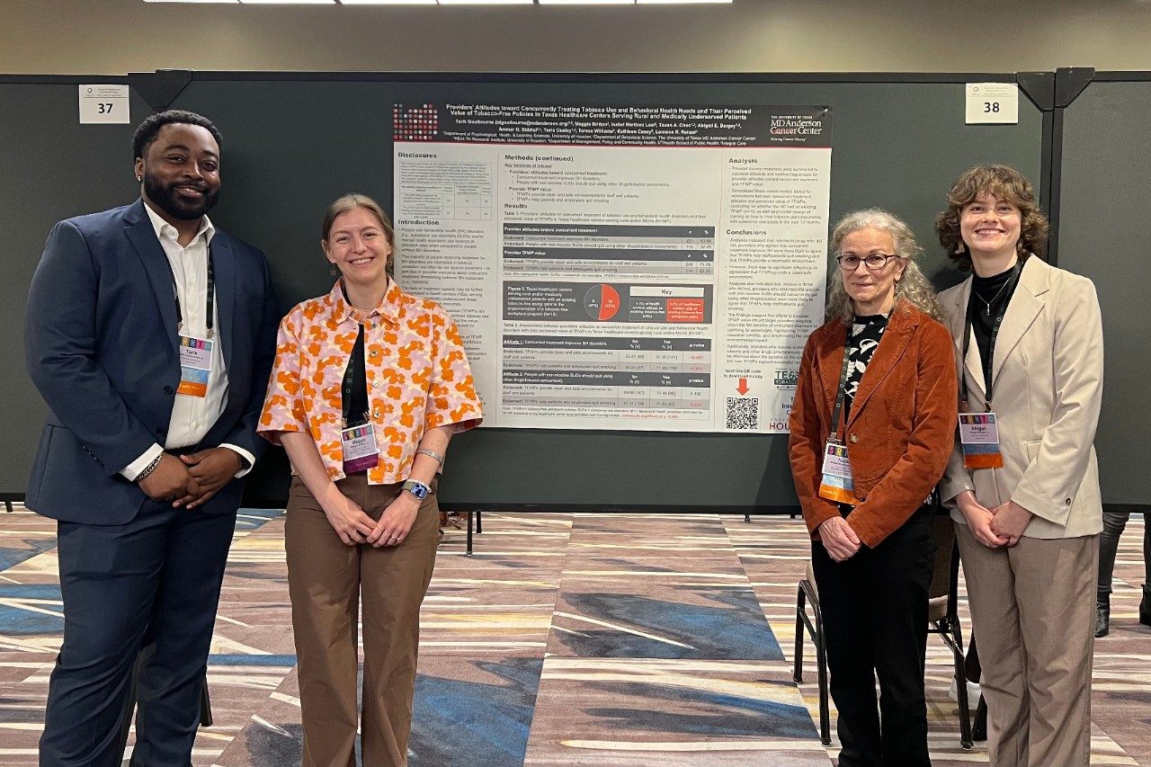 Four people posed around a poster, two on either side with the poster visible in between them