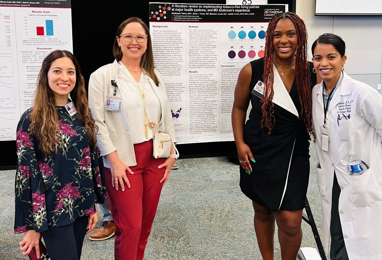 Four people posed in front of a scientific poster
