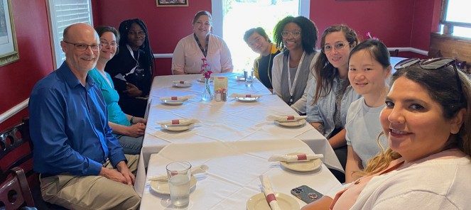Group photo of the Wood lab, seated at a long, tablecloth draped table, waiting for lunch as a reward for winning the 2022 Freezer Challenge