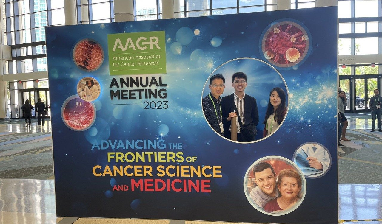 three people pose in a backdrop highlighting AACR