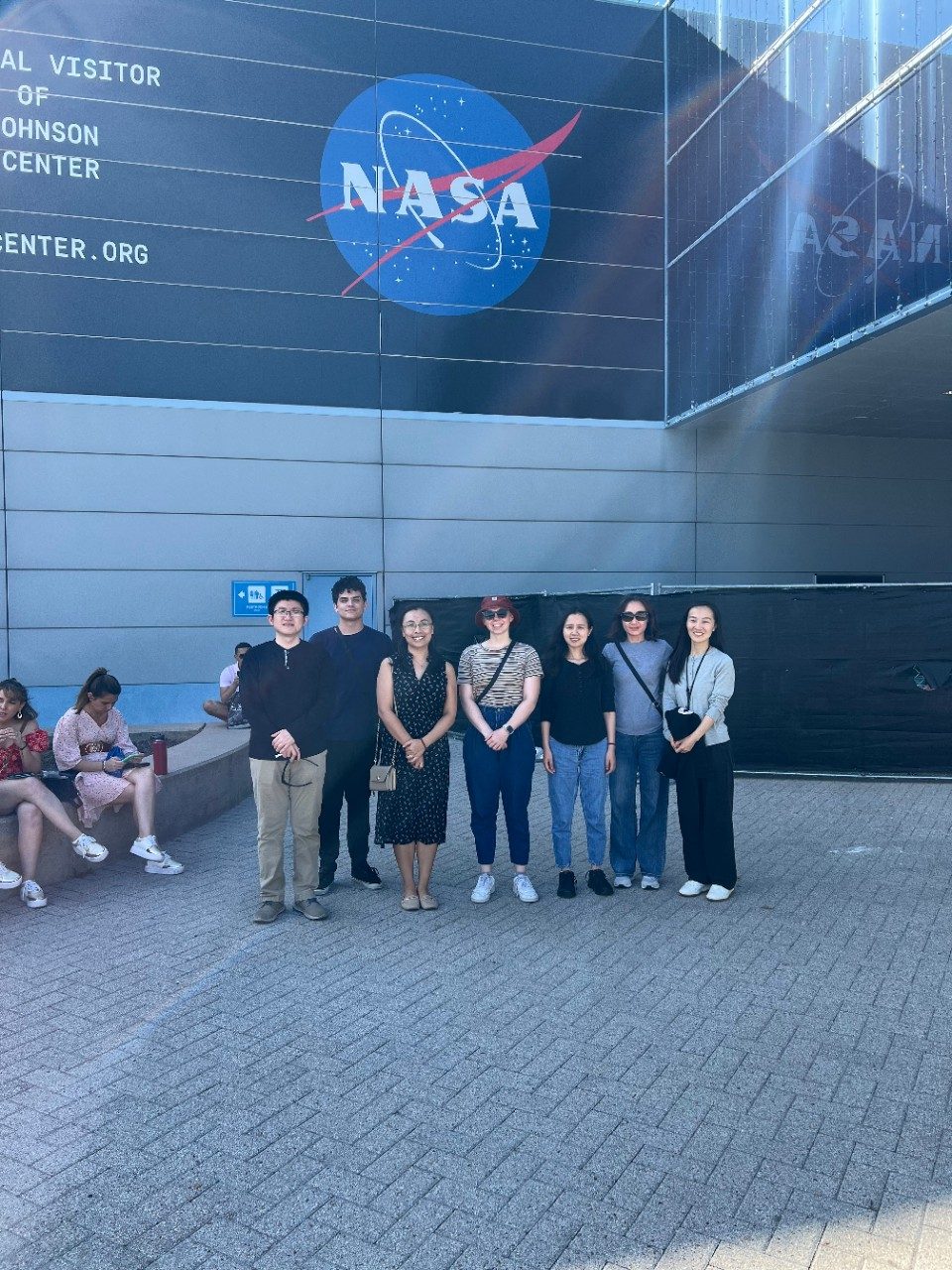 7 members of the Zhao Lab posing in front of the NASA logo on the outside of a building