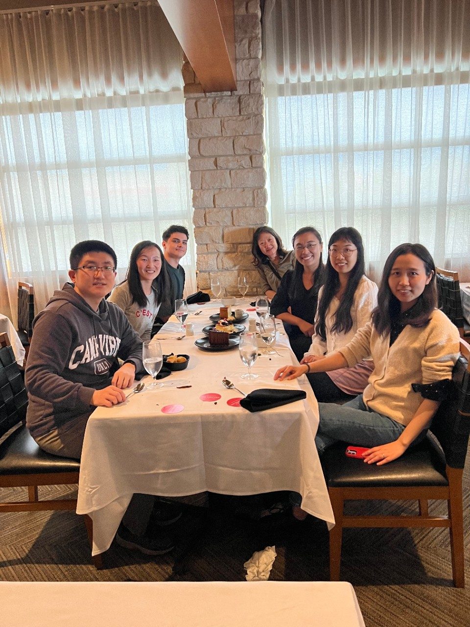 7 lab members sit around a rectangular restaurant table, smiling at the camera, with cake on the table