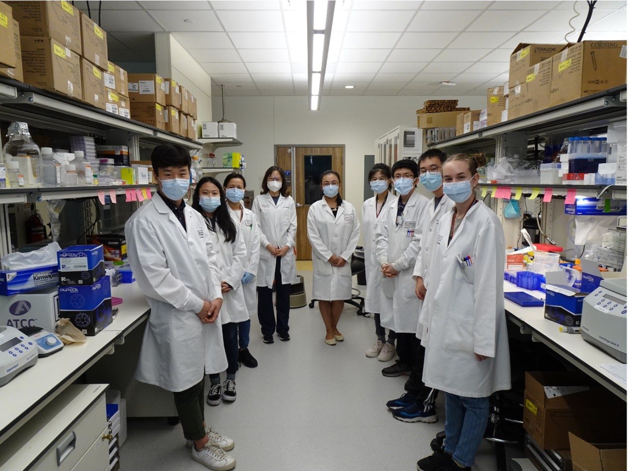 Group of people pose wearing masks and white lab coats in a wet lab area