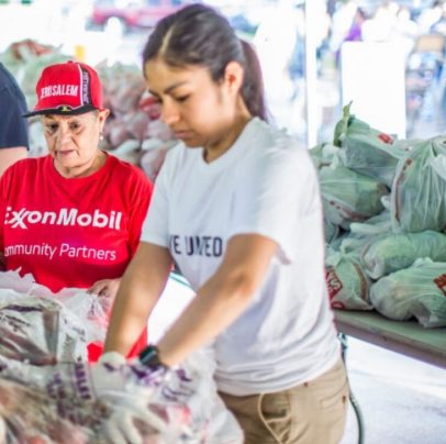 Two people, one in an ExxonMobil T-shirt, stand near a selection of produce