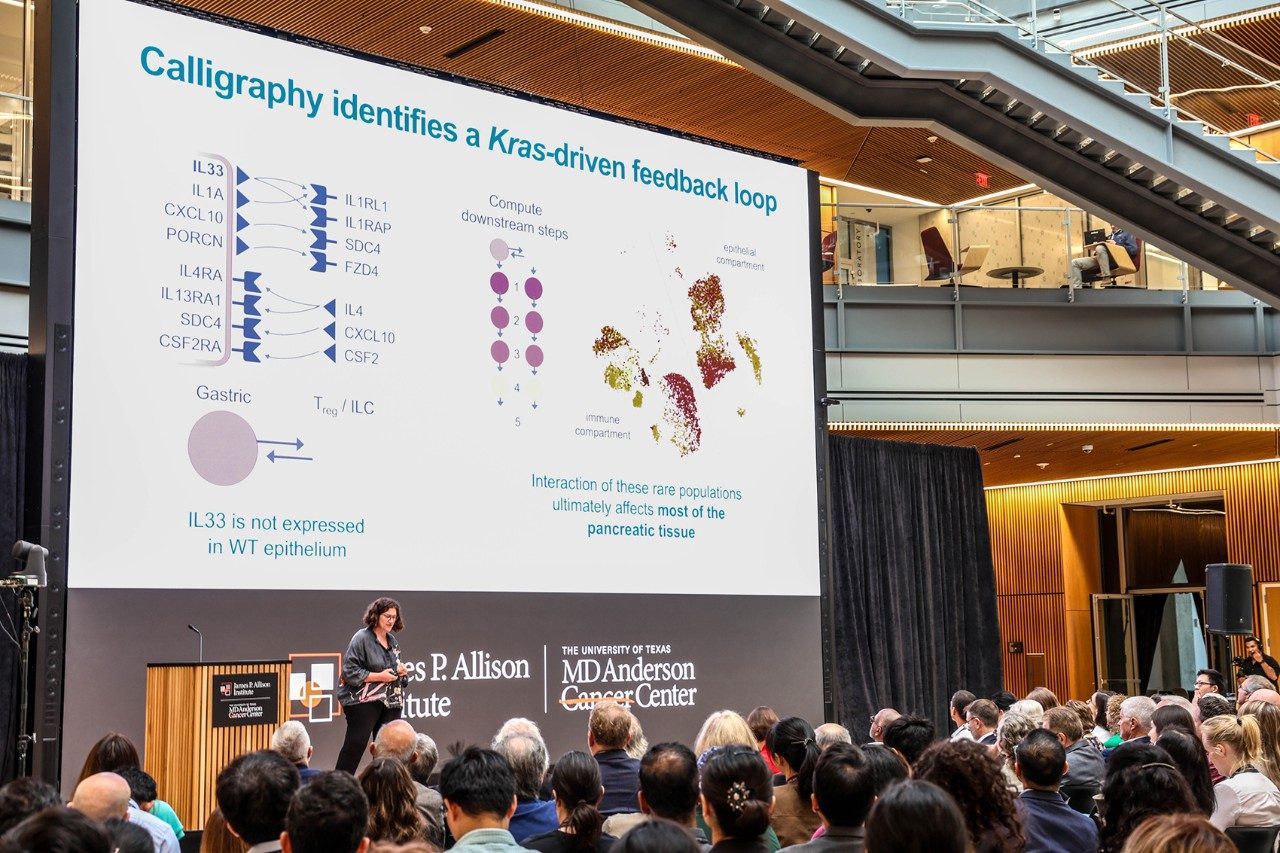A person standing on stage with a research slide behind