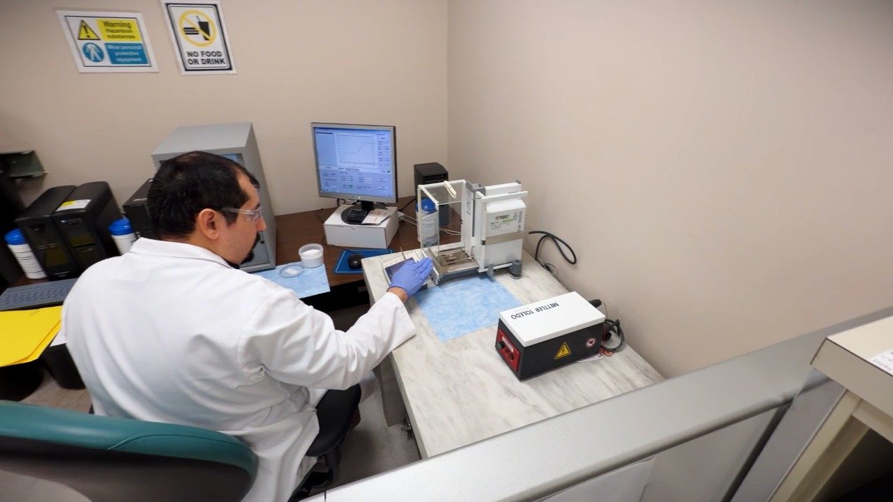 A man in a white coat sits a desk with instruments and a computer
