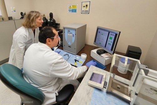 Two people in white coats look at a computer screen