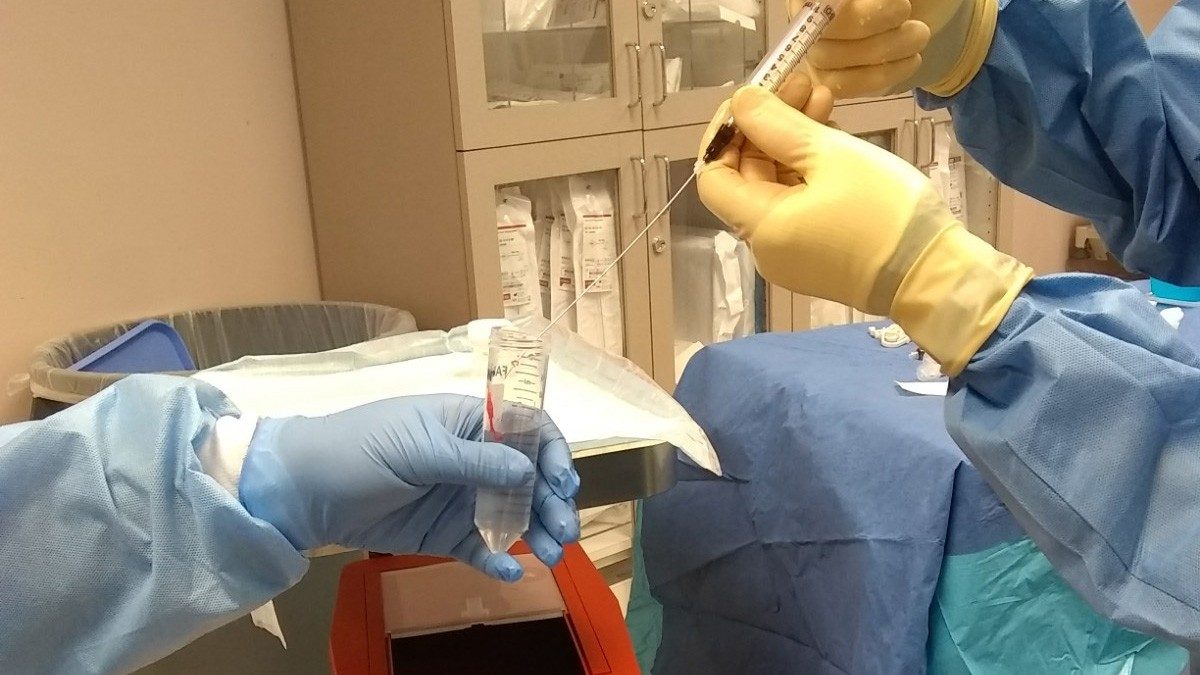 Two ITB staff members in protective gloves transfer liquid from a syringe to a tube.