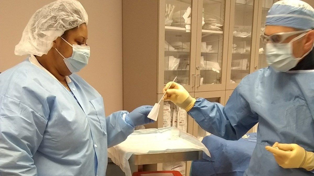 Two ITB staff members in protective gowns and gloves transfer a sample from a swab