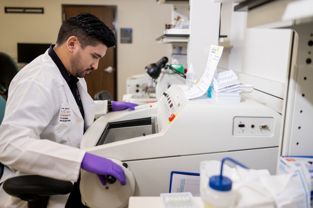 An RHCL staff member in a white coat and purple gloves prepares samples using a microtome