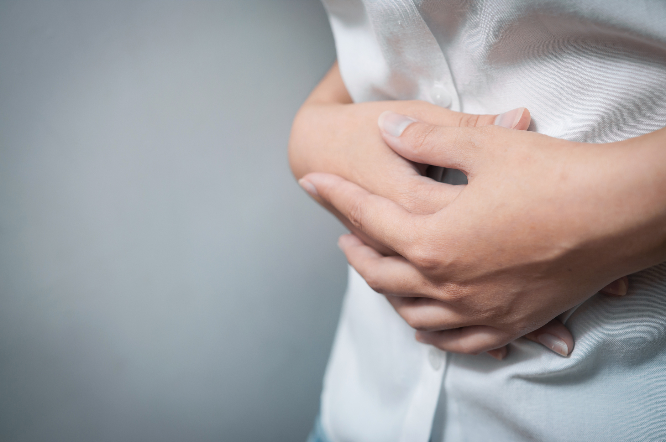 Close-up of a person clutching their lower abdomen, indicating abdominal pain or discomfort.